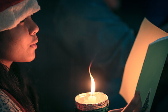 A children singer caroler hands holding candle and book with singing carol song on celebration of christmas day background