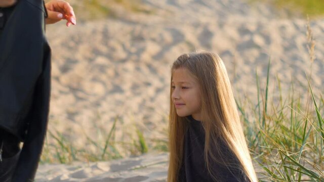 mom combs her daughter's hair sitting on the sand in nature