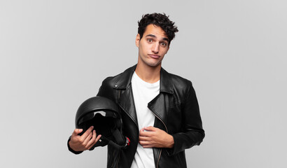 young handsome man shrugging, feeling confused and uncertain, doubting with arms crossed and...