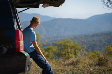 Young man is resting in nature with a car. Uses the trunk of an off-road vehicle for recreation