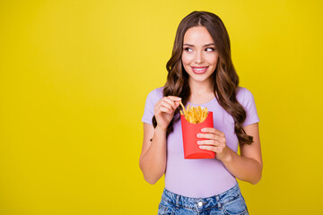 Portrait of attractive cheerful wavy-haired girl enjoying eating french fries copy space isolated...