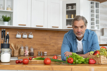 Grey-haired Mature handsome caucasian man standing in the bright kitchen.