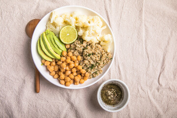 A bowl of healthy vegan and vegetarian lunch or dinner. Salad of fried chickpeas, quinoa, avocado, cauliflower on a light background.Top view, flat lay