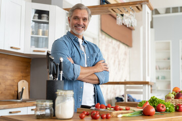 Grey-haired Mature handsome caucasian man standing in the bright kitchen.