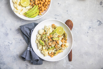 A bowl of healthy vegan and vegetarian lunch or dinner. Salad of fried chickpeas, quinoa, avocado, cauliflower on a light background.Top view, flat lay