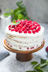 А piece of white cake with milk cream mousse and raspberry filling on a round transparent  stand.