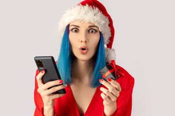 Naklejka premium Happy excited young woman in santa hat with gift box and smartphone