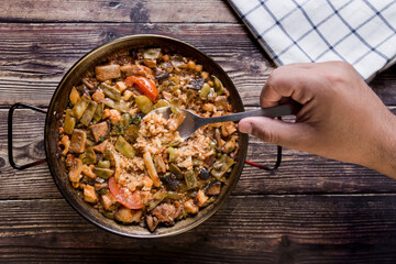 Hand with a spoon and in the background a paella