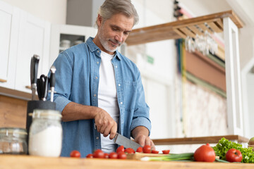 Grey-haired Mature handsome man preparing delicious and healthy food in the home kitchen