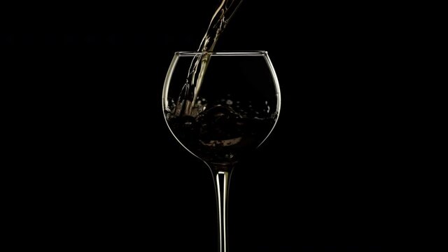 Pouring young white wine in slow motion black isolated background. Wine glass
