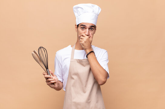 young baker man covering mouth with hands with a shocked, surprised expression, keeping a secret or saying oops