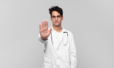 young physician looking serious, stern, displeased and angry showing open palm making stop gesture