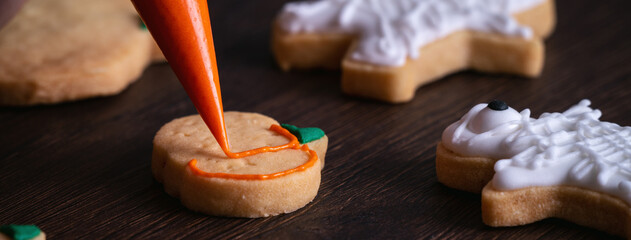 Close up of decorating cute Halloween pumpkin cookies with frosting in icing bag.