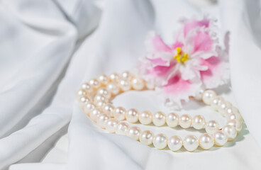 White pearl necklace on a white silk fabric. Holiday concept.