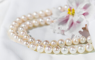 White pearl necklace on a white silk fabric. Holiday concept.