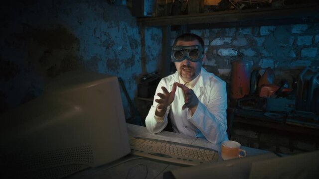Crazy scientist with stupid glasses records a video message in an old garage. Video conferencing with a funny researcher. Funny programmer with a mustache. Virtual, distance learning, teamwork from ho