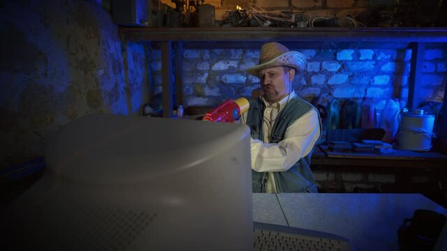 An adult mustachioed man is playing a children's computer game in a dark garage. Old PC shooters. A cowboy in a straw hat with a toy gun. Video games of the past generation. Duck Hunt. Retro. Vintage.