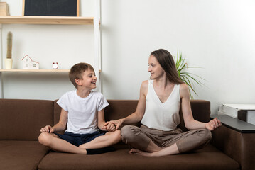 Fototapeta na wymiar Mom and son meditate while sitting on couch. Meditation at home with children.