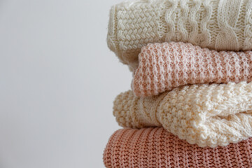 Bunch of knitted warm pastel color sweaters with different knitting patterns folded in stack, clearly visible texture. Stylish fall / winter season knitwear clothing. Close up, copy space for text.