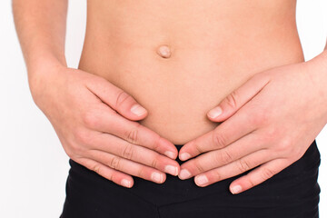 Young spotr girl suffering from stomach ache isolated on white background. Close up female person body in sportswear with pain in stomach. 