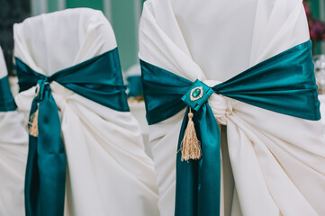 Row of beautiful chairs decorated with fabric and bows of green color in the wedding hall.