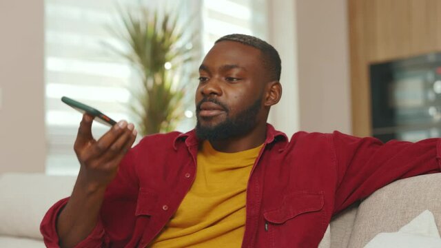 Close up african american young man recording voice message use phone in social network. Talking smiling using wifi indoors communicate technology microphone speaker. Slow motion