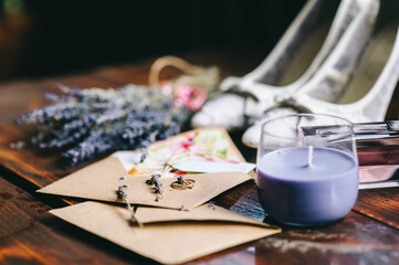 Wedding ring lies on a craft envelope next to a bouquet of lavender, candles and shoes.