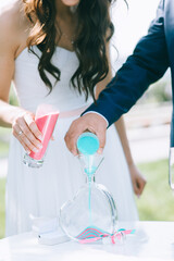 Close up of bride and groom pouring colorful sand into a glass vase in the shape of a heart.