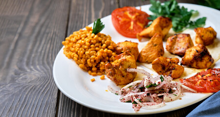 Light and delicious grilled chicken kebab, located on a platter with tomato and bulgur, decorated with cilantro sprigs. Healthy and tasty oriental cuisine. Close-up with copy space