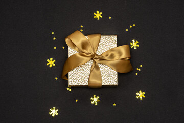 Gold gift box with ribbon and sparkling decorations on black background top view. New year and Christmas concept.