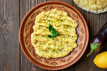 Grilled eggplant salad with garlic, lemon and olive oil in a clay bowl on a dark wooden background. Turkish salad of baked eggplant - patlıcan salata, top view