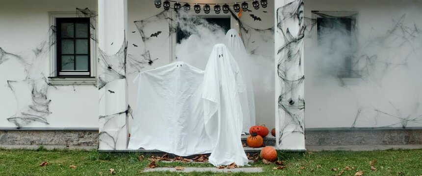 Funny family of four dressed as bedsheet ghosts posing on a porch of their house decorated for a Halloween celebration. Shot on RED Cinema camera with 2x Anamorphic lens