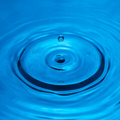 Water drop falling into water making a perfect droplet splash in blue