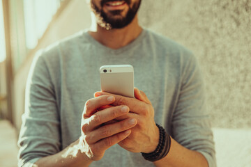 Young casual man using smartphone on the street. Wearing t-shirt and bracelets