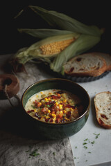 corn cream soup in a green plate on the table with corn and bread