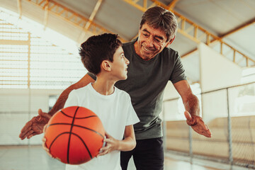 Latin grandfather and grandson playing basketball on the court