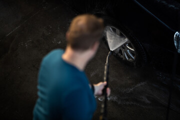 Young man washing his beloved car carefully in a manual car wash to prevent any damage and detail it properly
