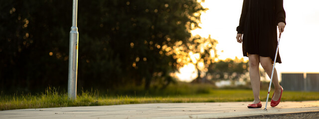 Blind woman walking on city streets, using her white cane to navigate the urban space better and to get to her destination safely
