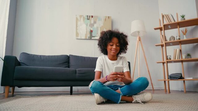 African american girl with crossed legs texting on cellphone at home