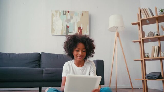 Smiling african american girl using digital tablet while sitting near couch