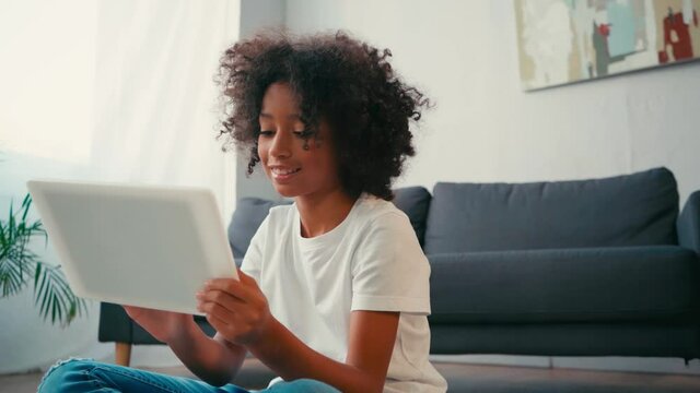 African american girl with crossed legs using digital while sitting near couch