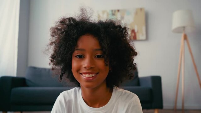 Selective focus of smiling african american girl looking at camera at home