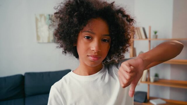 Selective focus of dissatisfied african american girl with thumb down at home