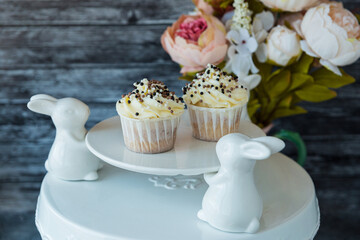 cupcakes with white cream decorated with balls of confectionery brown powder on a plate with rabbit-shaped legs