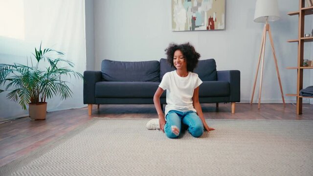 African american girl throwing ball to dog while sitting on carpet at home