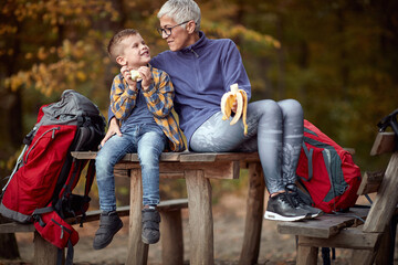 Grandmother and grandson eating the fruits  on the break of hiking in the forest