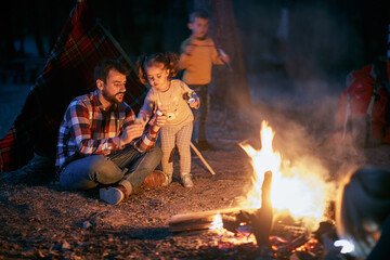Fototapeta premium Father and children having a good time around campfire in the forest