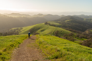 Lone hiker on a trail along a descending ridgeline with distance hills partially hidden in the fog...
