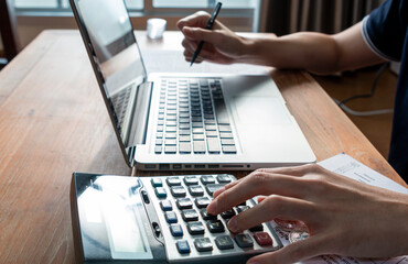 Close up of businessman or accountant hand on calculator to calculate and laptop, working on financial data report. Businessman working with calculator, business document and laptop computer notebook.