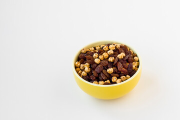 Double roasted yellow chickpeas and black raisins in yellow bowl on white,above view